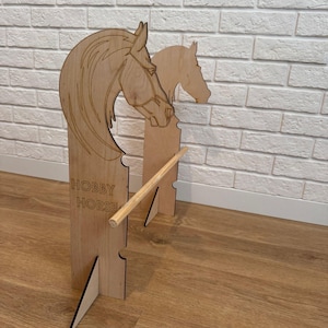 Könnte beinhalten: Ein hölzernes Steckenpferd mit einem braunen Holzsockel und einer braunen Holzstange. Der Pferdekopf ist aus Holz geschnitzt und hat eine braune Mähne und einen braunen Schweif. Der Pferdekopf ist nach links gerichtet. Die Worte "Hobby Horse" sind auf den Sockel geschrieben.