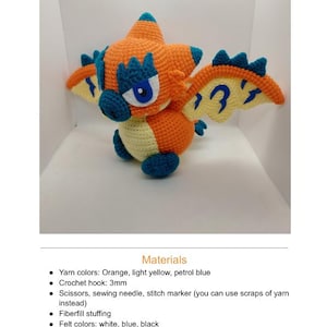 May include: A handmade crochet dragon toy in orange, light yellow, and petrol blue. The dragon has large blue eyes, wings, and a spiky head. The text "Rathalos" is at the top of the image.