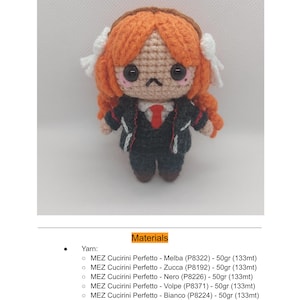 以下が含まれることがあります： 手作りのかぎ針編み人形、イシュマエル。オレンジ色の髪、黒いスーツ、赤いネクタイが特徴です。人形は大きな目をした詳細な顔をしており、白いリボンで飾られています。画像には、使用されている材料のリストも含まれています。