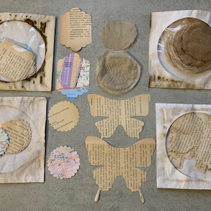 May include: Assortment of paper craft supplies, including circles, butterflies, and tags, all made from recycled book pages. The paper is beige and cream colored with black text.