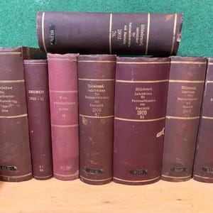 Puede incluir: Una colección de nueve libros antiguos de tapa dura con cubiertas marrones y letras doradas. Los libros se titulan "Jahrbücher für Nationalökonomie und Statistik" y "Bremen 1905-11".