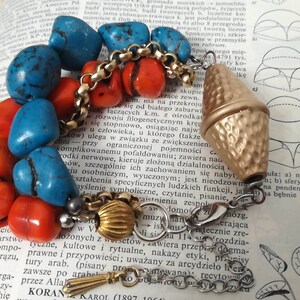 May include: A multi-strand bracelet featuring polished turquoise and orange stones, interspersed with gold-toned metal chain links. The piece includes a large, hammered gold-toned metal bead and a smaller ribbed gold-toned bead, finished with a lobster clasp.