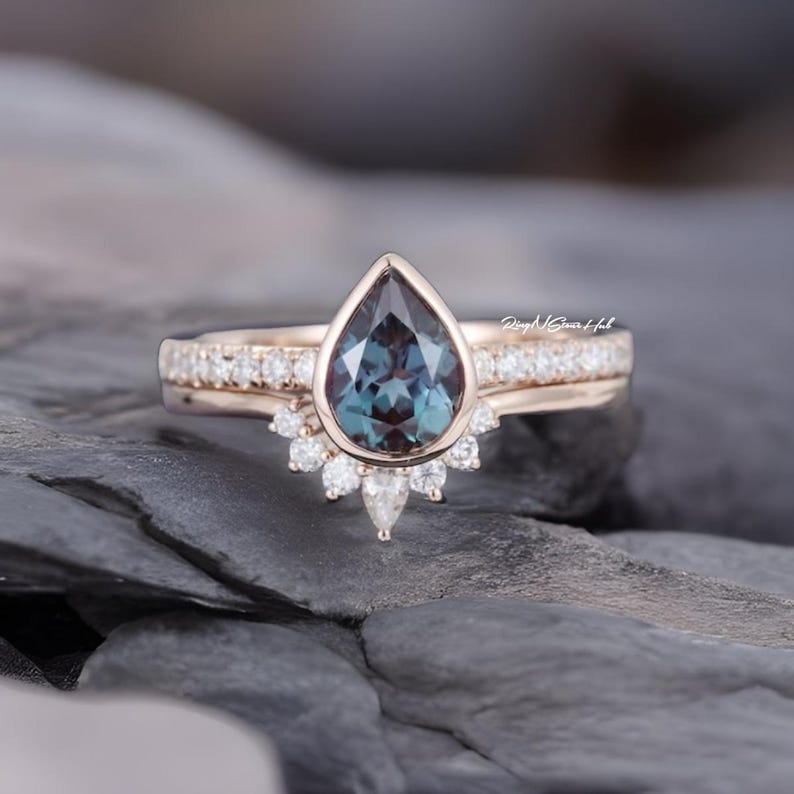 Pode incluir: Um conjunto de an&eacute;is em ouro rosa com uma pedra central em forma de pera que muda de cor, em um engaste de bisel. A banda &eacute; acentuada com pequenos diamantes redondos e um anel curvo com diamantes redondos e em forma de pera abaixo.
