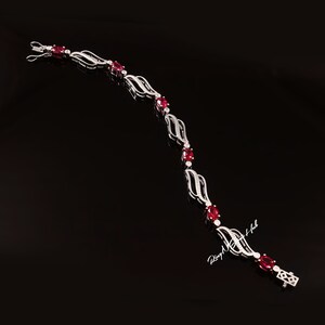 May include: A silver bracelet with a delicate, flowing design features red oval-shaped gemstones. The bracelet has a clasp closure.