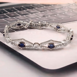 Könnte beinhalten: Ein silbernes Armband mit einem filigranen Design, das abwechselnd blaue ovale Edelsteine und kleinere klare runde Edelsteine aufweist. Das Armband hat einen Verschluss.