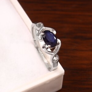 May include: A silver ring with a dark blue oval gemstone set in a delicate, twisted band.