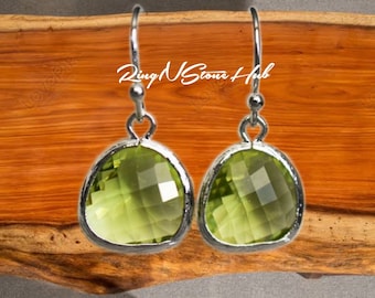 May include: A pair of silver dangle earrings with green gemstone drops. The earrings feature a teardrop-shaped green gemstone with a faceted design.