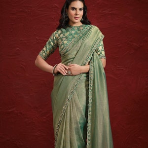 May include: A light green saree with a beaded border and a matching green blouse with a gold pattern. The saree is draped over a woman's body and has a tassel at the end of the border.