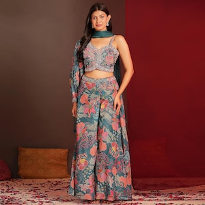 Puede incluir: Un conjunto con estampado floral turquesa que incluye un top corto con una manga larga, pantalones de pernera ancha y una bufanda a juego. El top tiene un corpiño con cuentas. El estampado floral incluye flores rosas, naranjas y blancas. El atuendo es adecuado para ocasiones especiales.