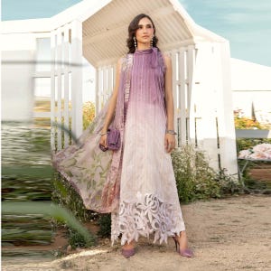 Op de afbeelding: Een lange, witte en paarse ombre-jurk met een kantversiering. De jurk heeft een hoge hals en is mouwloos. Het model draagt de jurk met een bijpassende sjaal met bloemenprint.