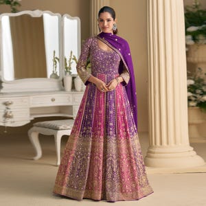 May include: A formal gown in shades of purple and pink, featuring intricate gold embroidery. The dress has a fitted bodice and a flowing skirt. A matching purple shawl drapes over the shoulders. The gown is suitable for special occasions.