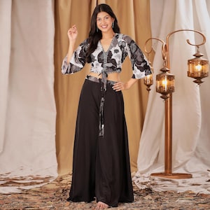 Pode incluir: Um conjunto de duas peças com um top curto com estampa floral e calças pretas de perna larga. O top tem decote em V e fecho de laço. As calças são de cintura alta e fluidas. O conjunto é adequado para uma ocasião casual ou semi-formal.