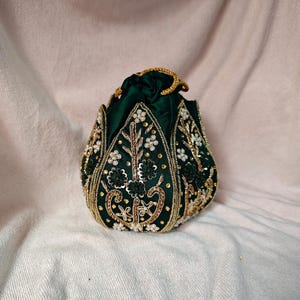 Detailed macro shot of the gold threadwork and the dark green base of the lotus clutch bag.