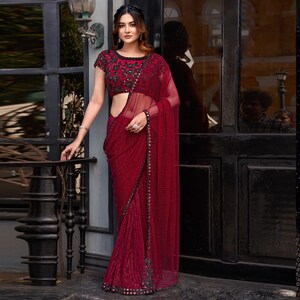 Könnte beinhalten: Ein maronfarbener Netz-Sari mit schwarzer Stickerei und Pailletten. Der Sari hat ein durchsichtiges Design und wird mit einer passenden schwarzen, bestickten Bluse kombiniert.