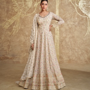 Puede incluir: Un vestido maxi blanco con estampado floral y una dupatta blanca a juego. El vestido tiene un escote en V y mangas largas. La dupatta está bordada con lentejuelas y tiene un borde festoneado.