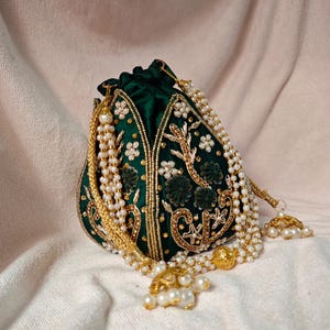 The green beaded clutch bag placed on a silk saree, highlighting its use as a traditional accessory.