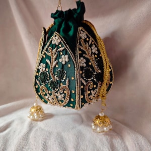 Flat lay of the dark green lotus potli bag next to fresh flowers and gold jewelry, showcasing its wedding style.