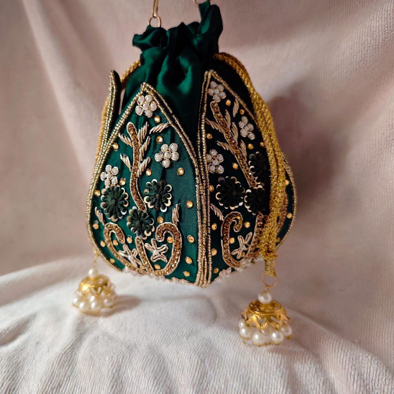 Flat lay of the dark green lotus potli bag next to fresh flowers and gold jewelry, showcasing its wedding style.