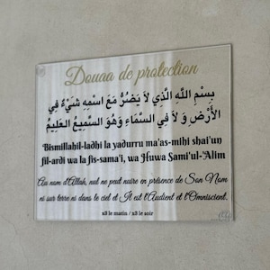 Może przedstawiać: Prostokątna, przezroczysta płyta akrylowa ze złotym tekstem. Tekst zawiera pismo arabskie, angielską transliterację i francuskie tłumaczenie. Płyta, zatytułowana "Douaa de protection", jest przeznaczona do ochrony.