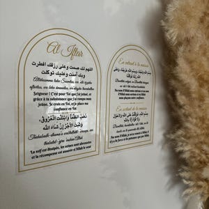Może przedstawiać: Dwa białe i złote dekoracyjne naklejki ścienne z tekstem arabskim i tłumaczeniami na język angielski. Tekst na lewej naklejce brzmi "Al Iftar", a tekst na prawej naklejce brzmi "En entrant à la maison" i "En sortant de la maison".