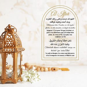 Może przedstawiać: Złota lampa z zapaloną świeczką stoi na stole, na którym leży sznur drewnianych koralików i białe kwiaty. Tekst w języku arabskim brzmi "Allahumma laka scumtou, wa ala rizqika oftartou, wa bika amanntou, wa alayka tawakaltou", co tłumaczy się jako "O Allah, dla Ciebie pościłem, a z Twojego daru złamałem swój post, i w Ciebie wierzę, i na Tobie polegam." Tekst brzmi również "Dhahaba al-dhamau wabtallatil-uraqu, wa thabat al-ajru inshaa Allah", co tłumaczy się jako "Pragnienie zniknęło, a żyły zostały nawilżone, a nagroda jest potwierdzona, jeśli Allah zechce."