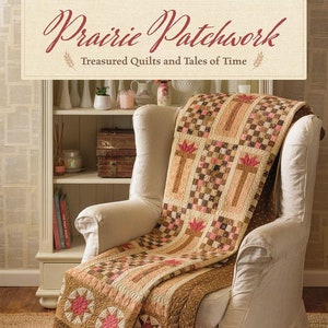 May include: A brown and tan patchwork quilt with red and pink accents is draped over a white armchair. The quilt is made with a variety of fabrics and patterns, including stars, flowers, and squares. The quilt is titled "Prairie Patchwork: Treasured Quilts and Tales of Time" by Martha Walker.