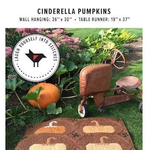 May include: A brown and beige quilt with a pattern of pumpkins. The quilt is on a bed of green grass. The text "CINDERELLA PUMPKINS" is at the top of the image. The text "WALL HANGING: 36" x 30" - TABLE RUNNER: 19" x 37" is below the title. A red toy wagon is in the background.