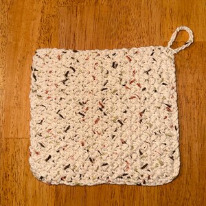 May include: A white crocheted pot holder with brown, green, and red flecks. The pot holder has a loop handle.