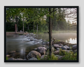 May include: A misty morning scene with a river flowing through a forest. The river is calm and still, with a few rocks in the water. The trees are tall and green, and the fog is thick and white.