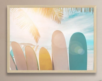 May include: A framed print of colorful surfboards leaning against each other on a sandy beach with a palm tree overhead and a bright blue sky.