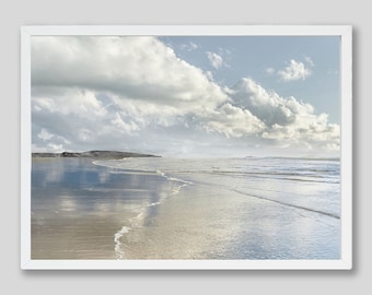 May include: A photograph of a beach with white sand and blue water. The sky is cloudy and the sun is shining. The water is calm and the waves are small. The beach is empty and there are no people in the photo.