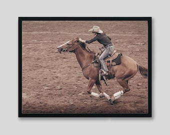 May include: A woman in a cowboy hat rides a brown horse in a rodeo arena. The horse is running and the woman is holding onto the reins. The arena is dirt and there are spectators in the background.