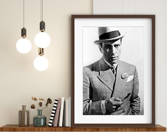 May include: Black and white photograph of a man in a suit and fedora. He is holding a cigarette in his right hand and looking directly at the camera.