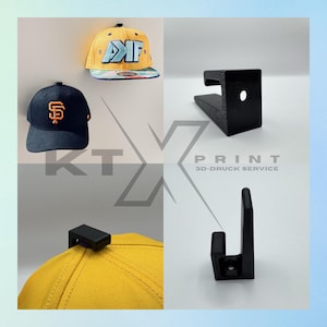 Könnte beinhalten: Ein Bild mit zwei Baseballkappen und zwei schwarzen 3D-gedruckten Huthaltern. Eine Kappe ist gelb mit blauen und weißen Akzenten, die andere marineblau mit einem orangefarbenen Logo. Die Halter sind zur Präsentation von Hüten konzipiert.
