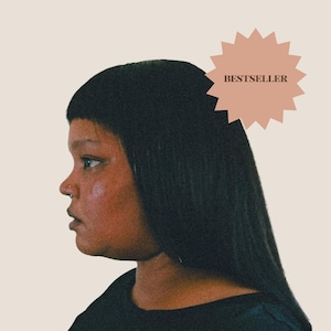 May include: A profile view of a person with straight black hair and bangs, wearing a black top. A light pink starburst-shaped graphic in the upper right corner contains the dark brown text BESTSELLER, indicating a popular item in the shop.
