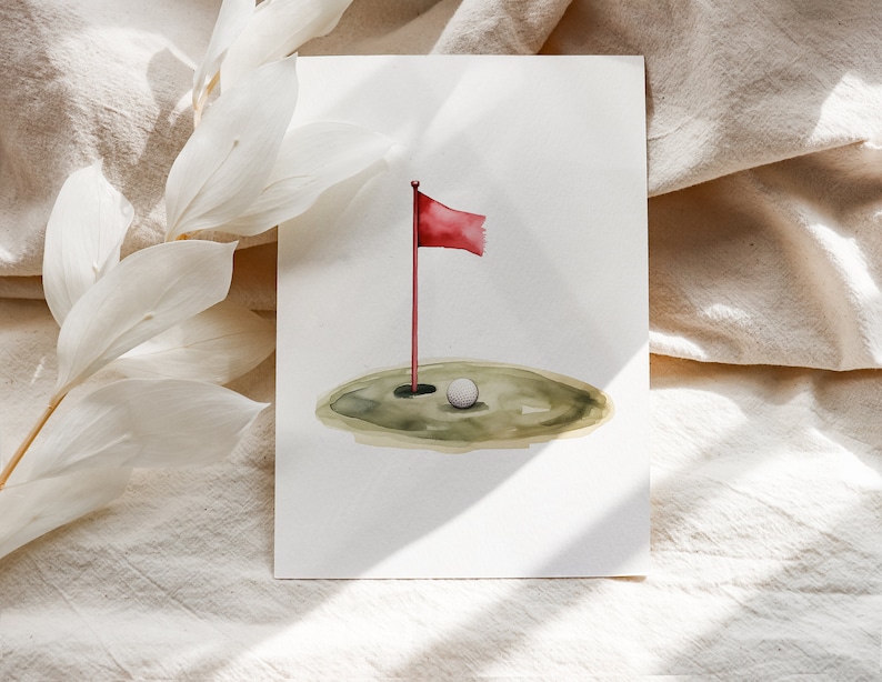 Puede incluir: Ilustraci&oacute;n en acuarela de una escena de golf. Una bandera roja ondea sobre un poste, marcando el hoyo. Una pelota de golf blanca descansa cerca del hoyo sobre un &aacute;rea verde y cubierta de hierba. La obra de arte est&aacute; sobre un fondo blanco.