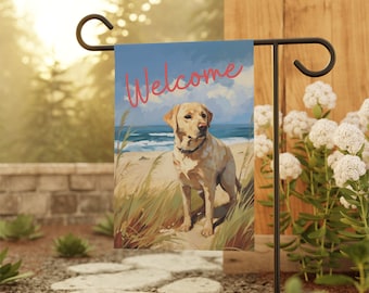 May include: A welcome garden flag with a yellow Labrador Retriever sitting on a beach. The flag has a blue sky with white clouds and the word "Welcome" written in red.