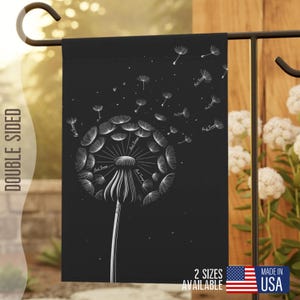 Könnte beinhalten: Schwarze Gartenflagge mit einem weißen Pusteblumen-Design. Die Pusteblume bläst Samen in den Wind. Die Flagge ist doppelseitig und trägt den Text "2 Größen verfügbar" und "Made in USA".