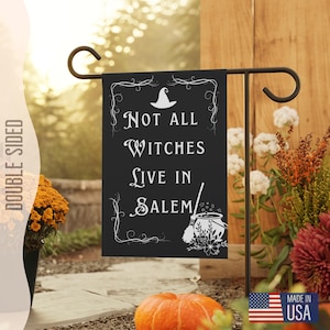 Może przedstawiać: Czarno-biała flaga ogrodowa z tekstem "Not all witches live in Salem" i ilustracją kapelusza czarownicy i kotła. Wyprodukowano w USA.