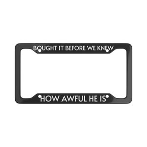 Op de afbeelding: Zwarte metalen kentekenplaathouder met witte tekst die "Bought it before we knew how awful he is." luidt.