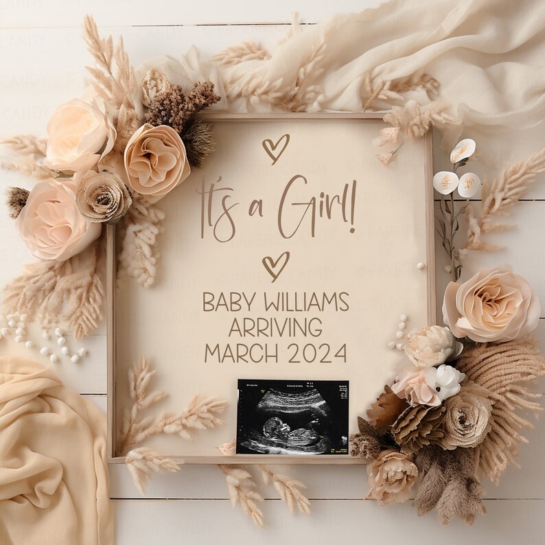 May include: A framed announcement with a neutral background, decorated with dried flowers and a small ultrasound image. The text reads "It's a Girl!" and "Baby Williams Arriving March 2024".