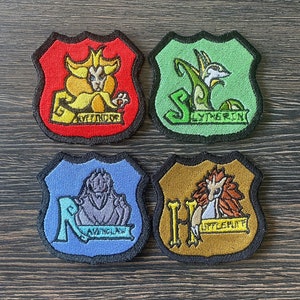Peut inclure: Quatre patchs brodés représentant les armoiries des maisons de Poudlard : Gryffondor, Serpentard, Serdaigle et Poufsouffle. Chaque patch présente un animal mascotte différent et le nom de la maison.