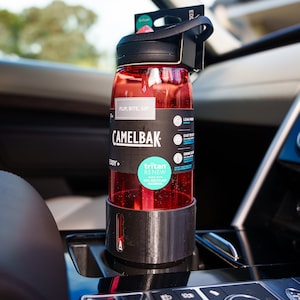 May include: A red CamelBak Eddy+ water bottle with a black lid and a black base. The bottle has a label that says "Flip, Bite, Sip" and "CamelBak". The bottle is sitting in a car cup holder.