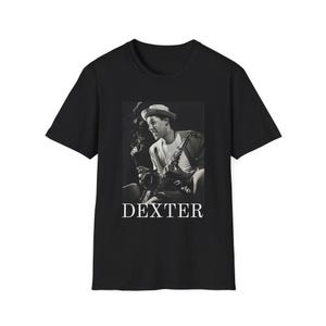 May include: Black t-shirt featuring a black and white image of a man playing a saxophone. The image includes the text "DEXTER" in white block letters at the bottom. The man is wearing a hat and appears to be smoking.