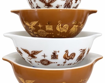 May include: A set of four nesting mixing bowls with handles, alternating between white and brown glass. The bowls feature a repeating brown graphic print of eagles, roosters, coffee grinders, and stars arranged around the exterior surface.