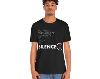 Puede incluir: Camiseta negra con texto blanco que dice "Nada fortalece la autoridad tanto como el SILENCIO" con una barra roja sobre un círculo blanco.