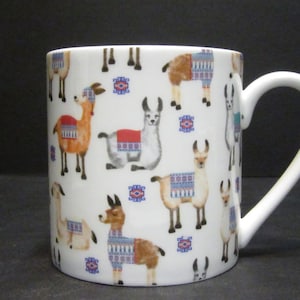 May include: White ceramic mug featuring a colourful llama pattern. The llamas are wearing colourful patterned blankets and are depicted in various poses.