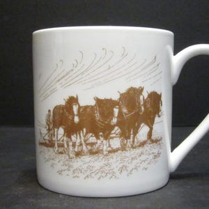 May include: White ceramic mug featuring a brown illustration of four horses pulling a plough. The mug has a brown handle.