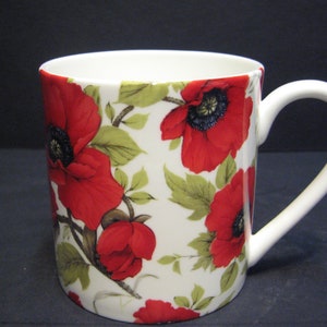May include: White ceramic mug with a red poppy floral pattern. The mug has a white handle.