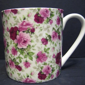 May include: White ceramic mug featuring a pink and burgundy floral design. The mug has a handle and is ideal for hot drinks.